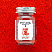 Burlap & Barrel - Noble Sweet Paprika - Single Origin Spice & Seasoning: 1.8 oz glass jar on paprika-covered surface, showcasing vibrant Hungarian spice from Kalocsa.