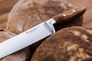 Wüsthof | Amici 9 Double Serrated Bread Knife placed on a loaf, showcasing its wooden handle and sharp blade, ideal for precise bread cutting.