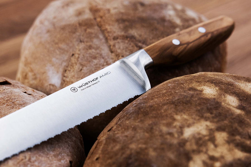 Wüsthof | Amici 9 Double Serrated Bread Knife placed on a loaf, showcasing its wooden handle and sharp blade, ideal for precise bread cutting.