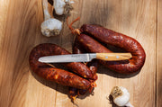 Wüsthof Amici 5 Serrated Utility Knife placed beside assorted sausages, showcasing its precision and versatility for culinary tasks.