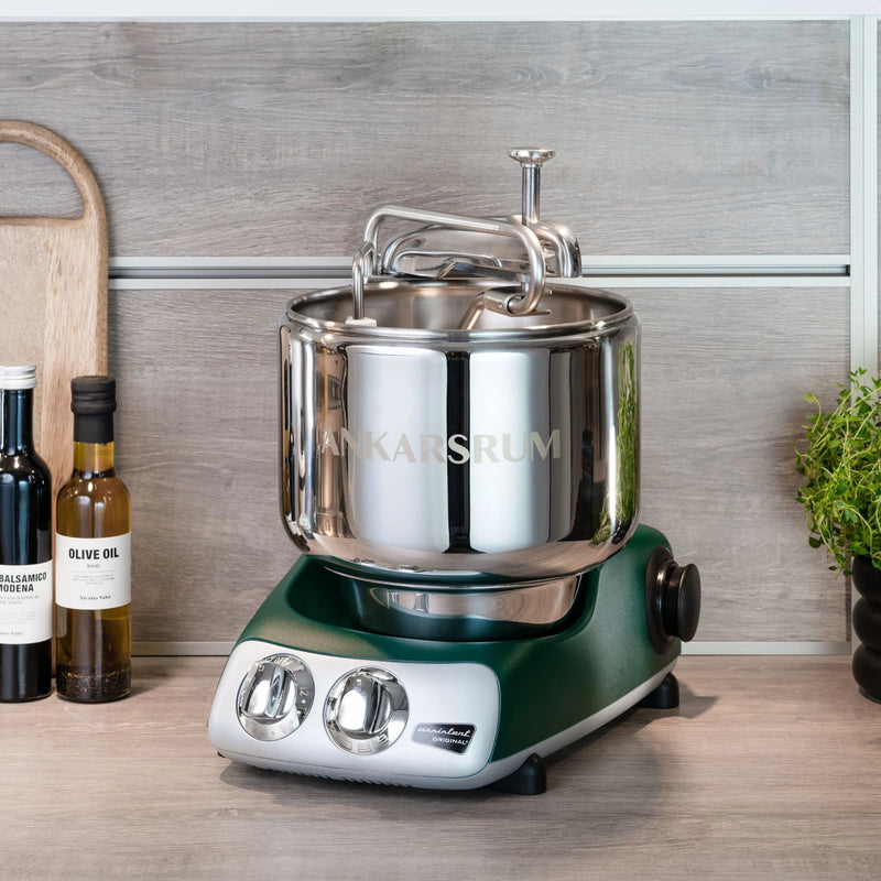 Ankarsrum | Stand Mixers: Retro green mixer with stainless bowl and attachments, perfect for heavy doughs, alongside olive oil, balsamico, and herbs on a wooden countertop.