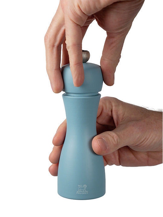 Hands opening a Peugeot | Tahiti Duo Salt + Pepper Mills, Air, showcasing its hourglass design, suitable for refilling, embodying elegance and functionality for any kitchen setting.