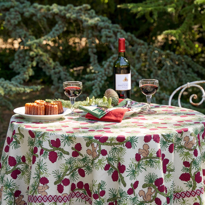 Couleur Nature - Squirrel and Pinecone Red & Brown Tablecloth on a garden table with wine, pastries, and pine centerpiece, showcasing French countryside charm.
