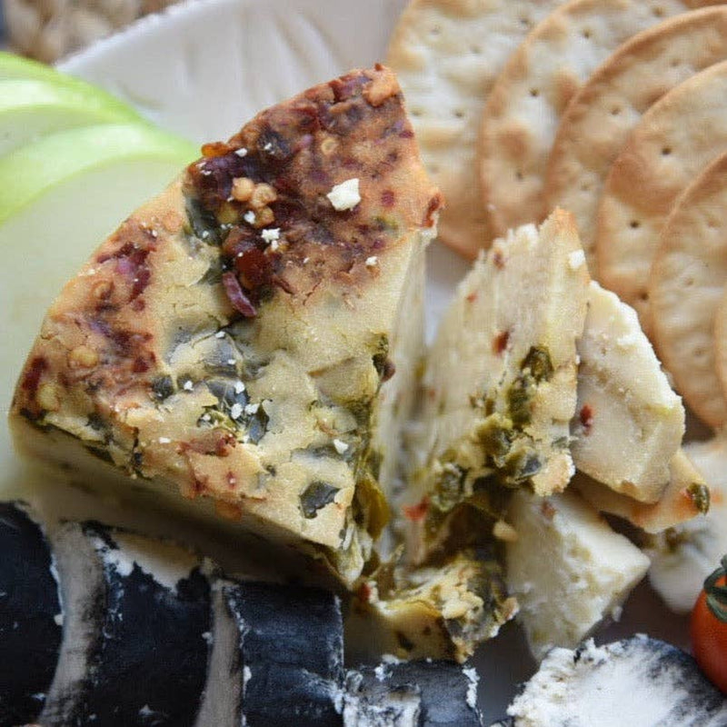 Rebel Cheese - Pepper Jack Plant Based, 5 oz, shown on a plate with crackers and a slice of green apple, highlighting its firm, sliceable texture.