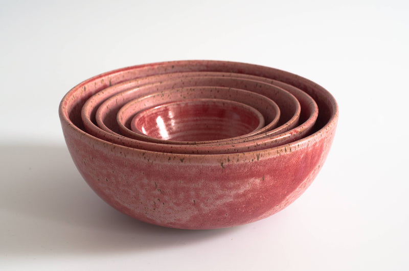 RachaelPots - Nesting Bowls Set of Five: A stack of handcrafted red ceramic bowls, ideal for versatile kitchen use, showcased in a kitchen store setting.