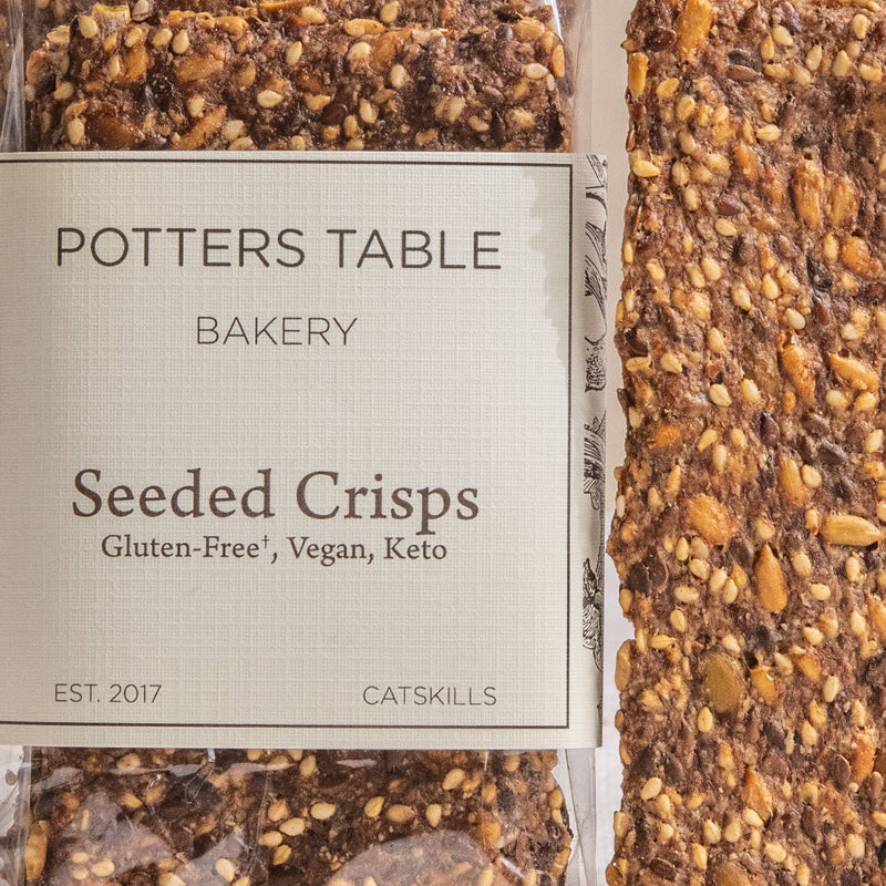 Potters Table - Gluten-Free Seeded Crisps: Thin, seed-studded crackers in clear packaging, gluten-free, vegan, keto-friendly, perfect for snacks or charcuterie, from Potter’s Table Bakery.