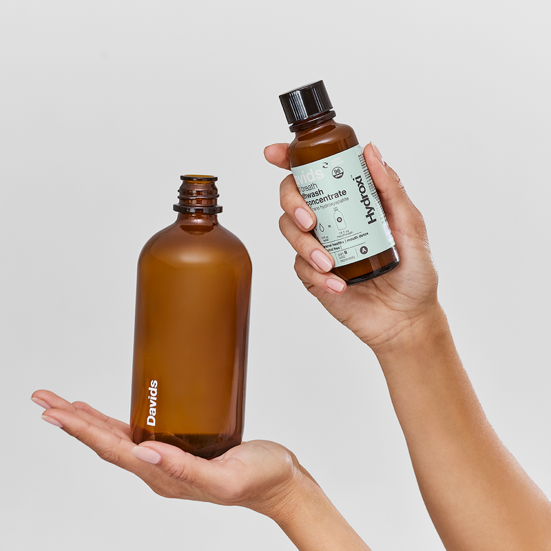 Hands holding Davids Hydroxi™ fresh breath mouthwash refill kit, featuring a 16oz reusable glass bottle and 4oz concentrate for sustainable dental care.