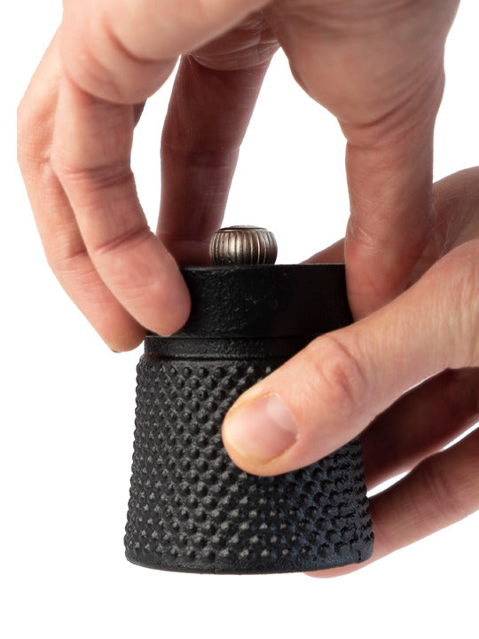 Hands adjusting the top knob of a Peugeot | Bali Cast Iron Pepper Mill, Black, showcasing its textured design and compact form, ideal for a refined pepper ceremony.