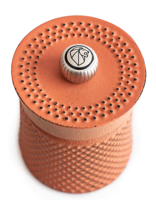 Peugeot | Bali Cast Iron Pepper Mill, Orange: Close-up of an orange, cylindrical pepper mill with vented top and embossed lion logo knob, inspired by traditional tea ceremonies.