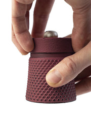Peugeot | Bali Cast Iron Pepper Mill in red, shown in hands, highlighting its textured cylindrical body and top knob, embodying traditional elegance from Athens Cooks.