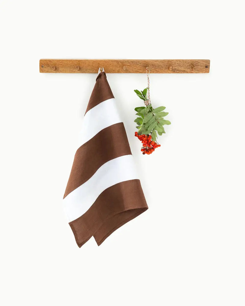 Striped linen tea towel hanging on a wooden bar, featuring a loop for easy hanging, part of MagicLinen's zero-waste program.