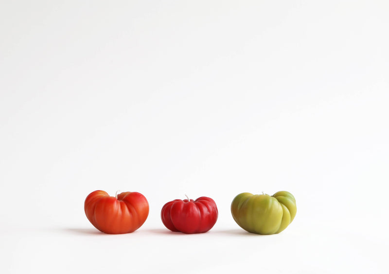 Artifaqt - Heirloom Tomato Beeswax Candle: Orange / Large, shaped like a tomato, displayed among real tomatoes, highlighting its artisanal craftsmanship and natural beeswax composition.
