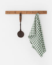 Linen tea towel on a hook, featuring a checkered pattern and a loop for hanging, next to a metal spoon with a wooden handle.