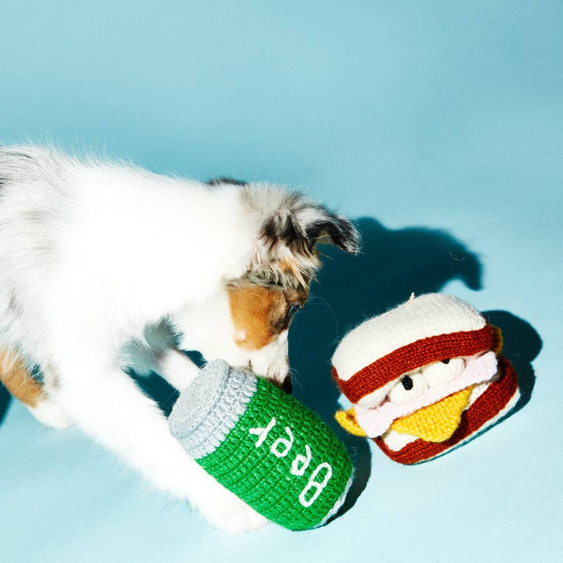 Puppy engages with Ware of the Dog Hand Knit Beer Dog Toy, made from fair-trade lambswool using natural dyes, offering a playful, ethical pet accessory.
