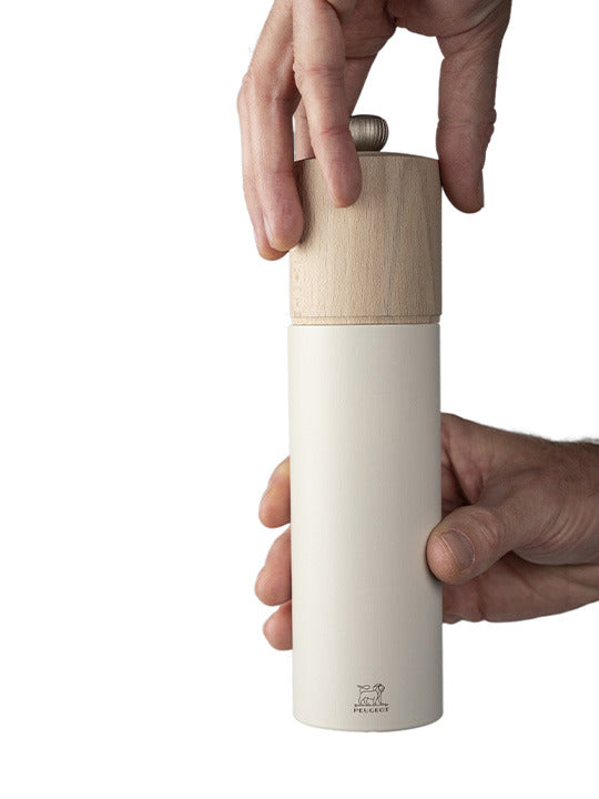 Hands twisting the top of a Peugeot | Boreal Salt Mill, Feather White, showcasing its sleek design and adjustable grind setting.