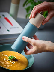 Hands holding Peugeot Boreal Salt Mill over a bowl of soup, highlighting the mill's elegant design and adjustable grinding mechanism for precise salt texture.