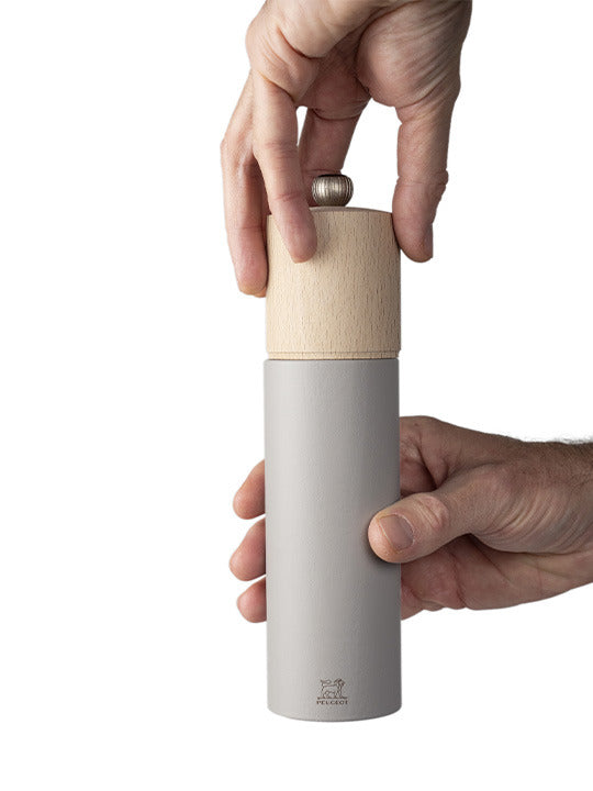 Peugeot | Boreal Salt Mills, Pebble Gray, with a light grey body and wooden top, shown in use with hands adjusting the grind mechanism.