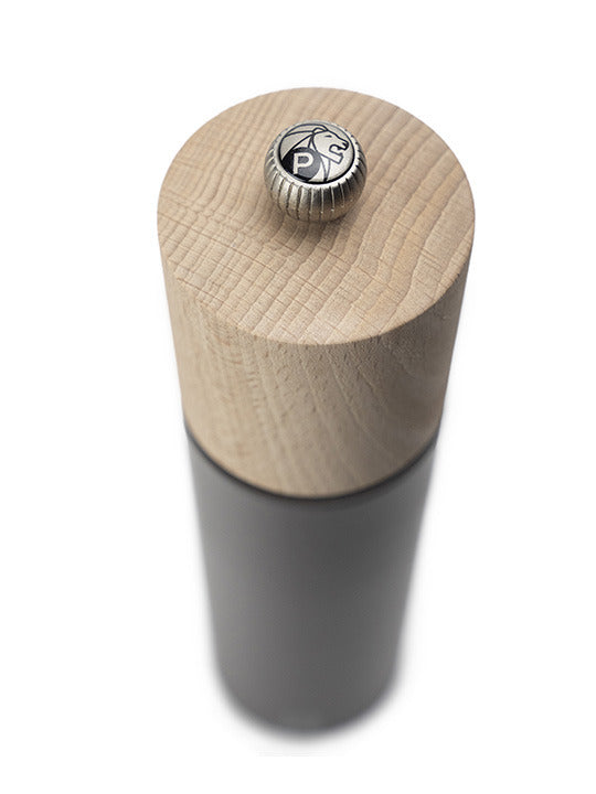 Peugeot | Boreal Pepper Mill, Rock Gray: A tall, cylindrical tabletop grinder with a natural wood top and dark metal body, featuring Peugeot's lion logo adjustment knob.