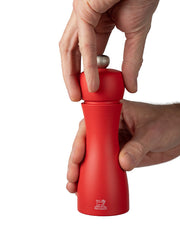 Peugeot | Tahiti Duo Salt + Pepper Mills, Fire: A hand twists the top knob of an hourglass-shaped red pepper mill, showcasing its ergonomic design and functionality.