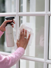 L'AVANT Collective - Fresh Linen Multipurpose Cleaner in a refillable spray bottle, held by a person cleaning a window, ideal for grease and grime removal.