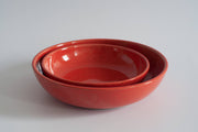 Two glossy, nested red-orange ceramic bowls from RachaelPots, perfect for pasta or noodles, on a light surface. Hand-thrown stoneware from Athens Cooks.