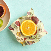 Bee's Wrap - Assorted 3 Pack - Meadow Magic, Plant Based Wax: floral-patterned wrap with halved orange, bowl with citrus fruits. Sustainable, reusable kitchen essential from Athens Cooks.