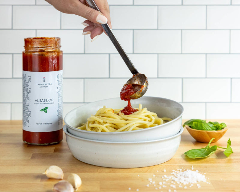 Zia Pia - Al Basilico Tomato Sauce by Italianavera drizzled over spaghetti, surrounded by garlic, salt, and basil, highlighting authentic Italian culinary tradition.
