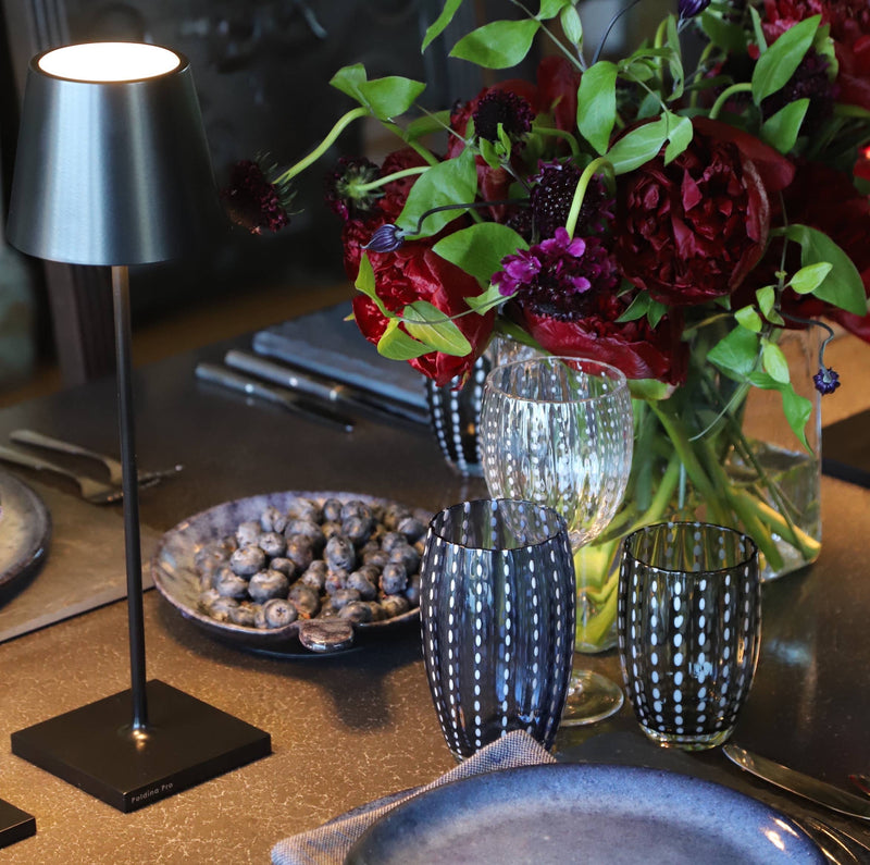 Zafferano America - Poldina Pro Cordless Lamp: Rust on a stylish table with blueberries, decorative glassware, and vibrant flowers, embodying modern elegance and functionality.