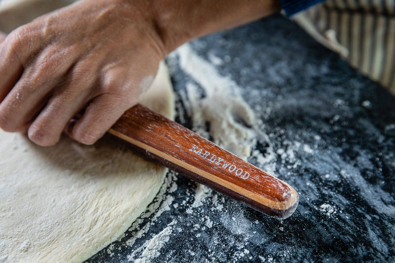 A person rolls dough with the Earlywood French Rolling Pin - Jatoba, showcasing its elegant, tapered silhouette designed for precision and control in baking.