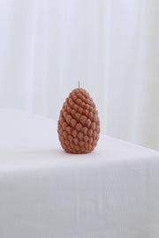 Mo&Co Home Exclusive Sculpted Beeswax Pine Cone candle on a white cloth, showcasing its intricate design, inspired by pine cones, available in two sizes for holiday elegance.
