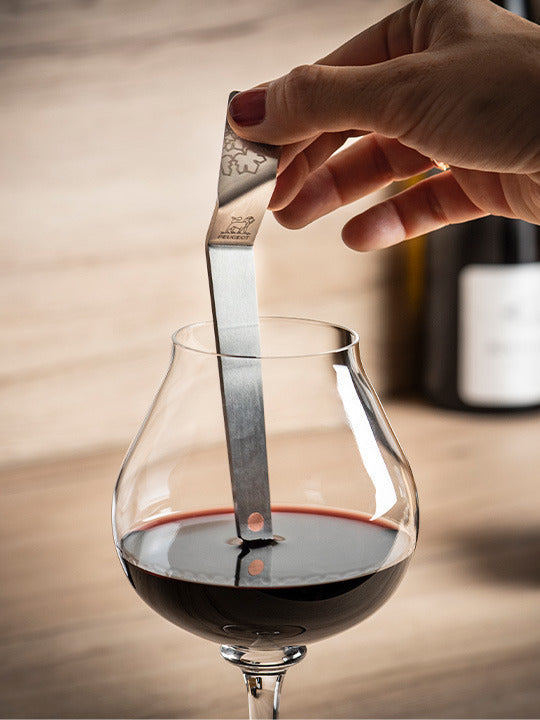 Peugeot Clef du Vin Wine Ageing Tool measuring wine's ageing potential in a snifter glass, held over wine bottles, exemplifying precision in wine tasting.