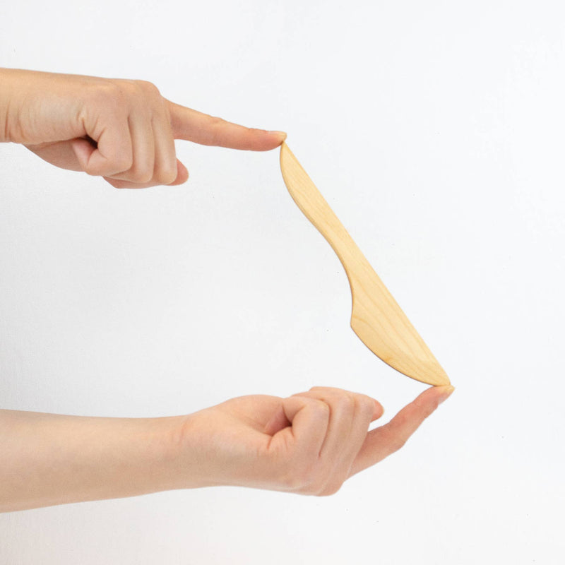 Two hands balance a Collin Garrity wooden spreader, ideal for soft cheese and jam, against a white background. Perfect for enhancing any kitchen experience.