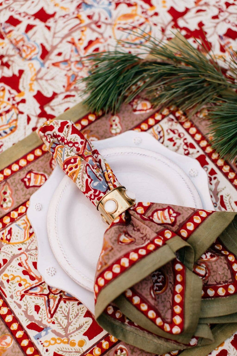 Couleur Nature - Noel Red/Green Napkins on a scalloped plate with gold napkin ring, set on a festive tablecloth, perfect for holiday gatherings.