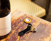 L'Atelier du Vin - USA - Chromed Foil Cutter for Wine Bottles, shown on a wooden table with a multi-tool corkscrew and wine capsule cutter.