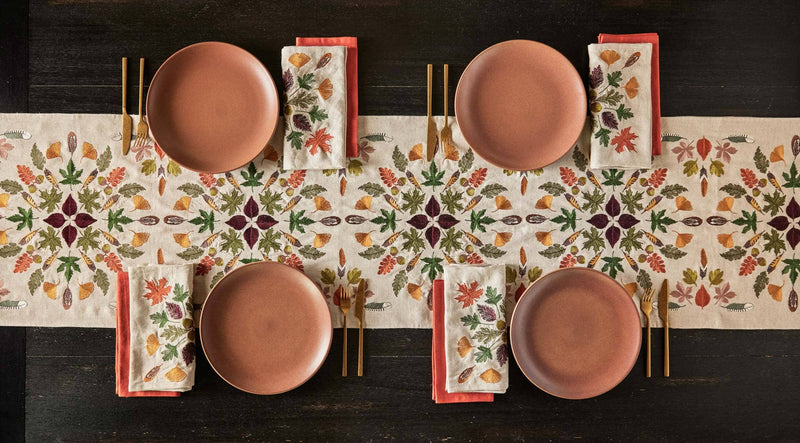 Coral & Tusk - Pressed Leaves Dinner Napkin elegantly folded on a terracotta plate, featuring embroidered autumn leaves, acorns, and quail feathers, enhancing a fall-themed table setting.