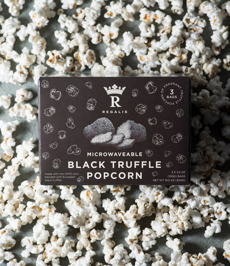 Regalis Foods | Microwave Black Truffle Popcorn Box with 3 bags, surrounded by freshly popped popcorn, offering gourmet convenience with non-GMO corn and European Black Truffles.