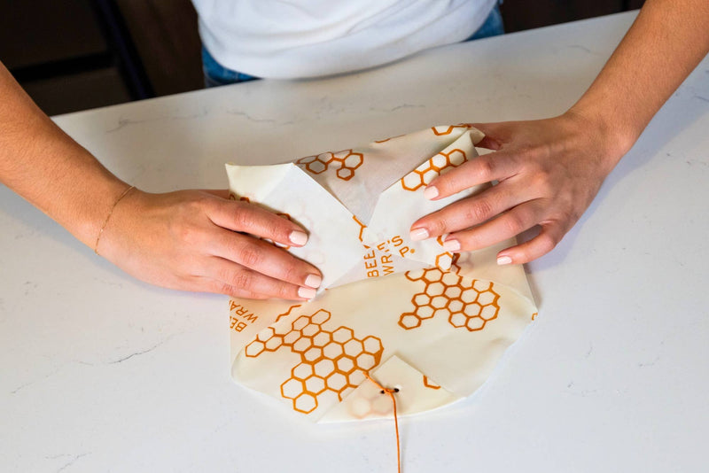 Hands wrapping Bee's Wrap - Lunch 3 Pack - Honeycomb Print, showcasing reusable sandwich and snack wraps for eco-friendly food storage.