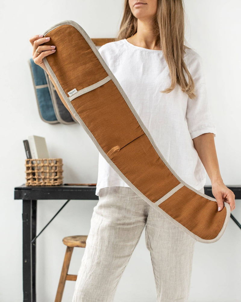 A woman holds MagicLinen's cinnamon gingham double oven mitt, designed for safe cooking, part of a sustainable, zero-waste kitchen accessory line.