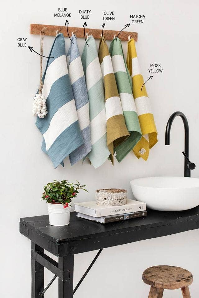 Striped linen tea towel with loop, displayed on a bathroom sink alongside towels and a plant, showcasing its practicality and design.