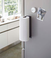 Yamazaki Home Magnetic Steel Paper Towel Holder, White, attached to a stainless-gray fridge, holding a roll of paper towels in a modern kitchen setting.