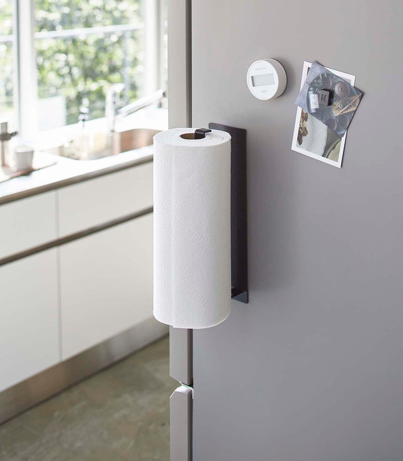 Yamazaki Home Magnetic Steel Paper Towel Holder, White, attached to a stainless-gray fridge, holding a roll of paper towels in a modern kitchen setting.