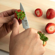 Shun Classic Paring Ebony Knife, 3.5 inches, skillfully hulls a strawberry on a wooden board, showcasing precision and versatility in kitchen tasks.