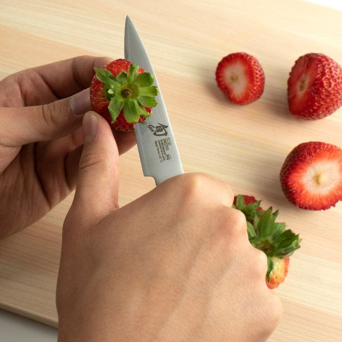 Shun Classic Paring Ebony Knife, 3.5 inches, skillfully hulls a strawberry on a wooden board, showcasing precision and versatility in kitchen tasks.