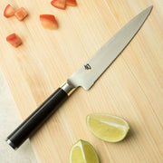 Shun Classic Serrated Utility Knife, 6-inch, on a wooden board with diced tomatoes and lime wedges, showcasing its versatility for precise slicing tasks.