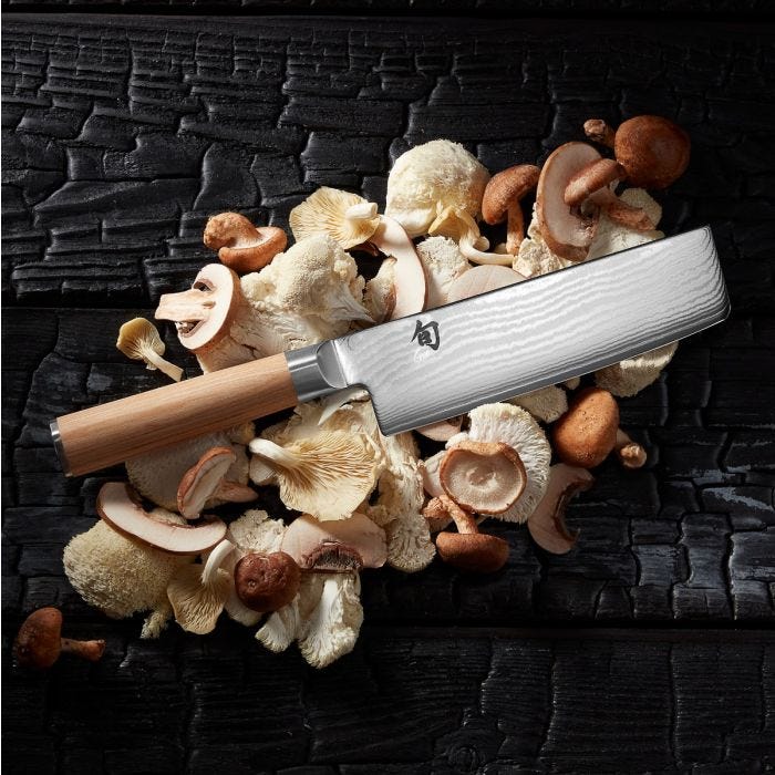 Shun | Classic Blonde Nakiri, 6.5 inches, showcases its Damascus-steel blade and wooden handle, elegantly placed on a bed of fresh mushrooms.