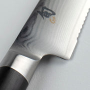 Shun Classic Serrated Utility Knife, 6 inches: Close-up of blade with Damascus layers, scalloped edge, meeting bolster, and D-shaped wooden handle. Ideal for precise slicing tasks.