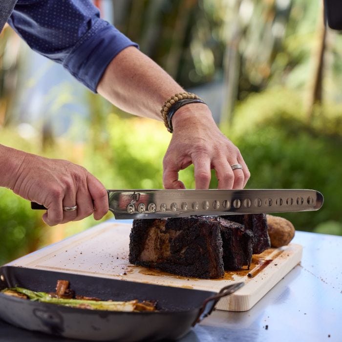 A close-up of the Shun Classic Hollow Ground Brisket Knife slicing a seasoned roast on a wooden board, showcasing its precision and craftsmanship.