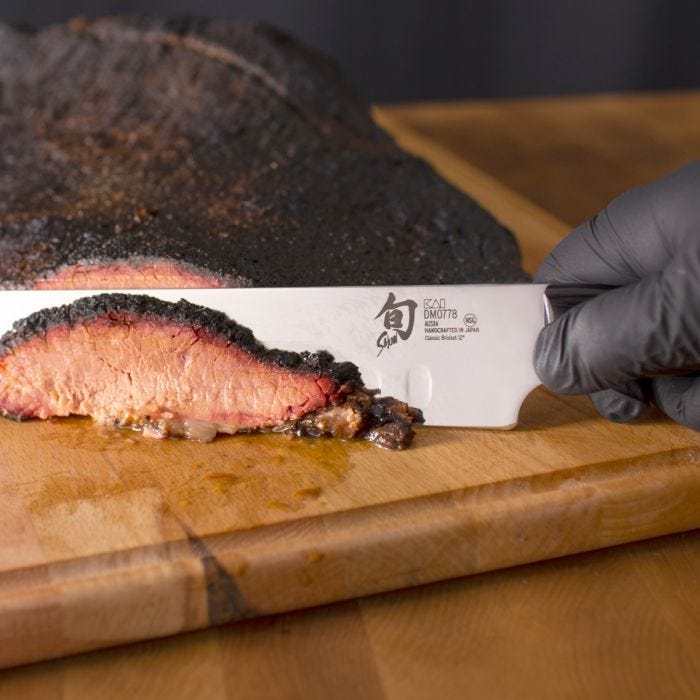 Shun Classic Hollow Ground Brisket Knife effortlessly slices a smoked beef brisket, showcasing its sharp blade and precision, ideal for culinary enthusiasts.