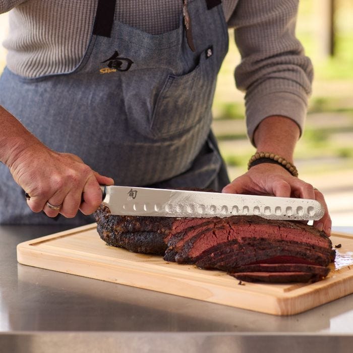 Person slicing roast with Shun Classic Hollow Ground Brisket Knife, ideal for precise meat cuts, available at Athens Cooks, a specialty kitchen store in Athens, Georgia.