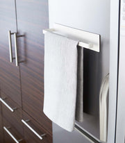 Yamazaki Home Magnetic Steel Paper Towel Holder, White, mounted on a fridge, holds a gray towel, showcasing minimalist, space-saving design for efficient kitchen organization.